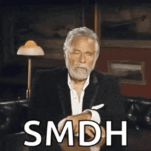 a man with a beard is sitting at a table with the word smdh written on the table .