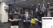 three men are looking at papers in a gym and one of them is wearing a shirt that says muscle cool
