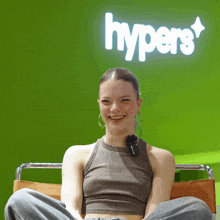 a woman sits in front of a green wall with the word hypers on it
