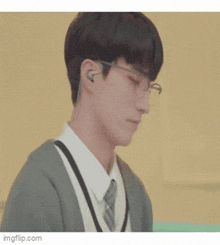 a young man wearing glasses and ear buds is sitting in a room .