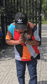 a man wearing a black adidas hat and a colorful shirt