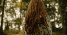 a woman with long red hair stands in front of trees
