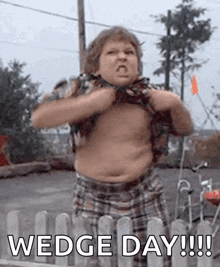 a fat boy is standing in front of a fence with his shirt off and making a funny face .