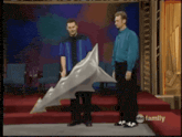 two men standing on a stage with a shark shaped object in front of them with abc family in the corner