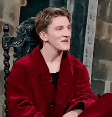 a young man is sitting in a chair wearing a red jacket .