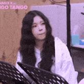 a girl with long black hair is sitting in front of a sign that says nmixx in go tango