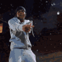 a man in a white sweatshirt and white shorts is pointing at the camera at night .