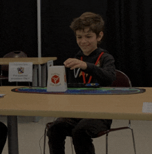 a boy sits at a table with a cup that says cube head on it