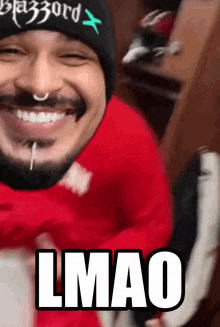 a man with a beard wearing a beanie and a red sweater is smiling and says lmao