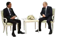 two men in suits are sitting at a table with a bouquet of flowers on it