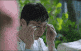 a man in a hospital gown adjusts his glasses in front of a green background