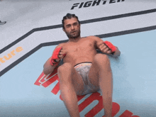 a shirtless fighter is sitting on a mat with fighter written on the wall behind him