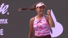a woman wearing a pink tank top and a visor is standing in front of a screen that says mx