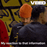 a man wearing an orange beanie talks to another man with the words my reaction to that information below him
