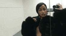 a woman in a fur coat is taking a selfie in front of a mirror