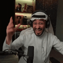 a man wearing headphones and a head scarf is sitting in front of a microphone and smiling