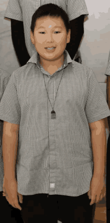 a young boy wearing a plaid shirt and a necklace smiles for the camera