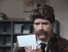a man with a mustache holds a piece of paper that says ja