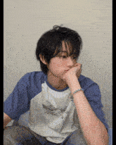 a young man wearing a blue and white t-shirt has his hand on his face