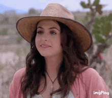 a woman wearing a straw hat and a pink cardigan is smiling ..