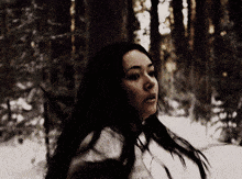 a woman with long black hair is standing in a forest