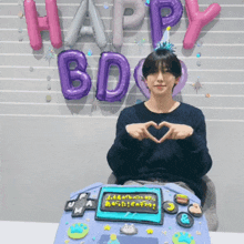 a man making a heart shape with his hands in front of balloons that say happy birthday