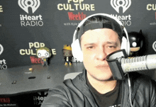 a man wearing headphones stands in front of a microphone in front of a wall that says iheart radio