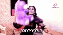 a woman is sitting on a couch holding a purple stuffed animal .