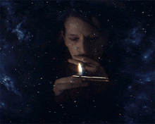 a man is lighting a cigarette with a lighter in front of a starry sky