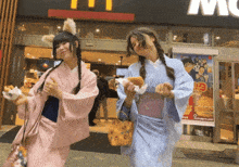 two women in kimonos are standing in front of a mcdonald 's restaurant