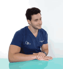 a man wearing a blue scrub top with om written on the front sits at a table