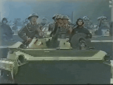 a group of soldiers are riding on top of a tank and one of them is wearing a helmet with the letter a on it