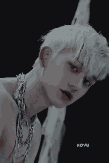a close up of a man with white hair and a necklace around his neck .
