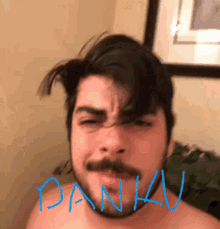 a shirtless man with a beard and mustache is making a funny face with the name daniav written on his face