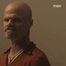 a man with a beard and a red shirt is standing in front of a wall that says max