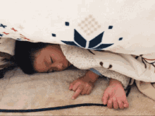 a child is laying under a blanket with a blue and white pattern