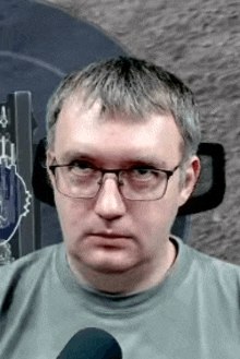 a man wearing glasses and a grey shirt is sitting in a chair .