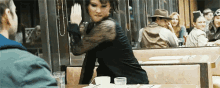 a woman in a black dress is sitting at a table in a restaurant talking to a man .