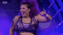a woman with purple hair is standing in front of a purple background with her arm in the air .