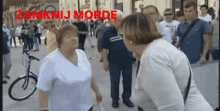 two women are standing next to each other on a street with the words zamknij morde written in red
