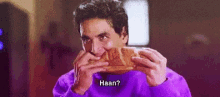 a man in a purple sweater is eating a piece of bread and says `` haan '' .