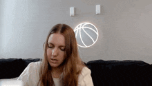 a woman sits on a couch in front of a neon basketball sign
