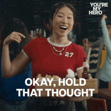 a woman wearing a red shirt with the number 27 on it says okay hold that thought