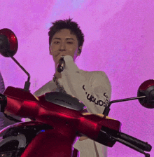 a man singing into a microphone while riding a red honda motorcycle