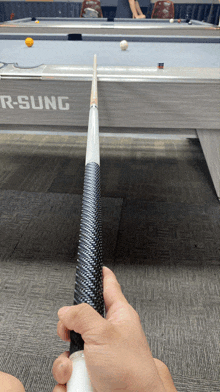 a person holding a pool cue in front of a pool table that says r- sung