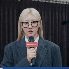 a woman wearing glasses and a suit is holding a microphone with a sign that says babymonster