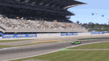 a green race car is driving down a race track with a stadium in the background