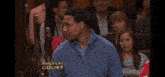 a man in a blue sweater is sitting in front of a paternity court screen