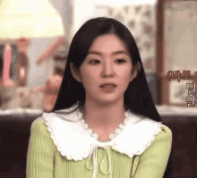a woman with long black hair is wearing a green sweater with a white collar .