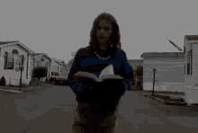 a woman in a blue and red sweater is holding a book in front of a row of mobile homes